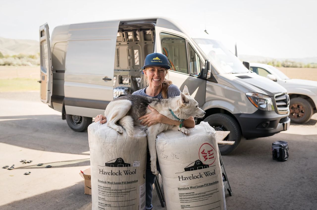 Woman holding her dog beside a camper van and bags of Havelock Wool insulation